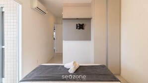 A modern hotel room with a bed, a towel, a wall-mounted air conditioner, and a sliding door. - IAPs Apto 140m da praia Floripa (Florianópolis)