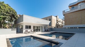 A modern outdoor swimming pool area with a building in the background. - IAPs Apto 140m da praia Floripa (Florianópolis)