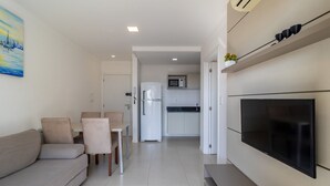 A modern living room with a flat-screen TV, a sofa, and a dining area with chairs. - IAPs Apto 140m da praia Floripa (Florianópolis)