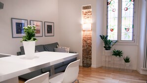 A modern living room with a dining area, featuring a white table, grey sofa, and a brick accent wall. - Italianway - Copernico I (Milan)