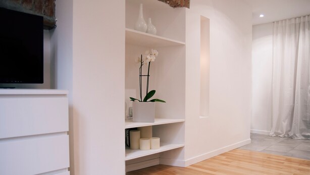 A modern living room with a flat-screen TV, white shelving with decorative items, and a wooden floor. - Italianway - Copernico I (Milan)