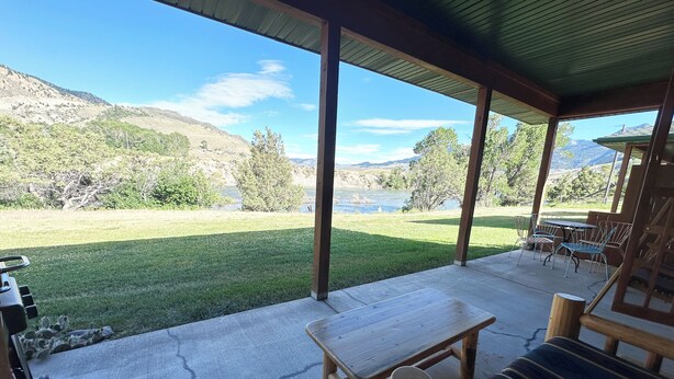 A covered patio with a view of a lake and mountains, wooden furniture, and a table. - 
Charming Riverside Cabin on Yellowstone River - 2 Bedrooms & 2 Bathrooms, Relax (Gardiner)