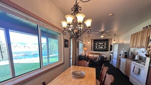 A dining area with a wooden table and chairs, a chandelier, and a view of the outdoors. - 
Charming Riverside Cabin on Yellowstone River - 2 Bedrooms & 2 Bathrooms, Relax (Gardiner)