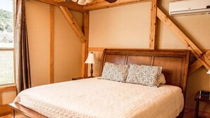 A bedroom with a wooden bed frame, a white quilted bedspread, patterned pillows, a bedside lamp, and a thermostat on the wall.