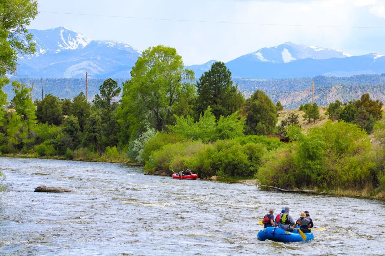 A river with a raft and a red boat, surrounded by trees and mountains.