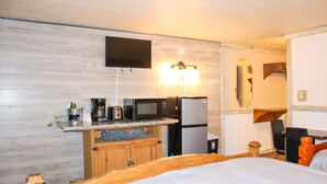 A compact hotel room with a bed, kitchenette, and a TV mounted on the wall. - Black Bear Lodge 4 (Howard)