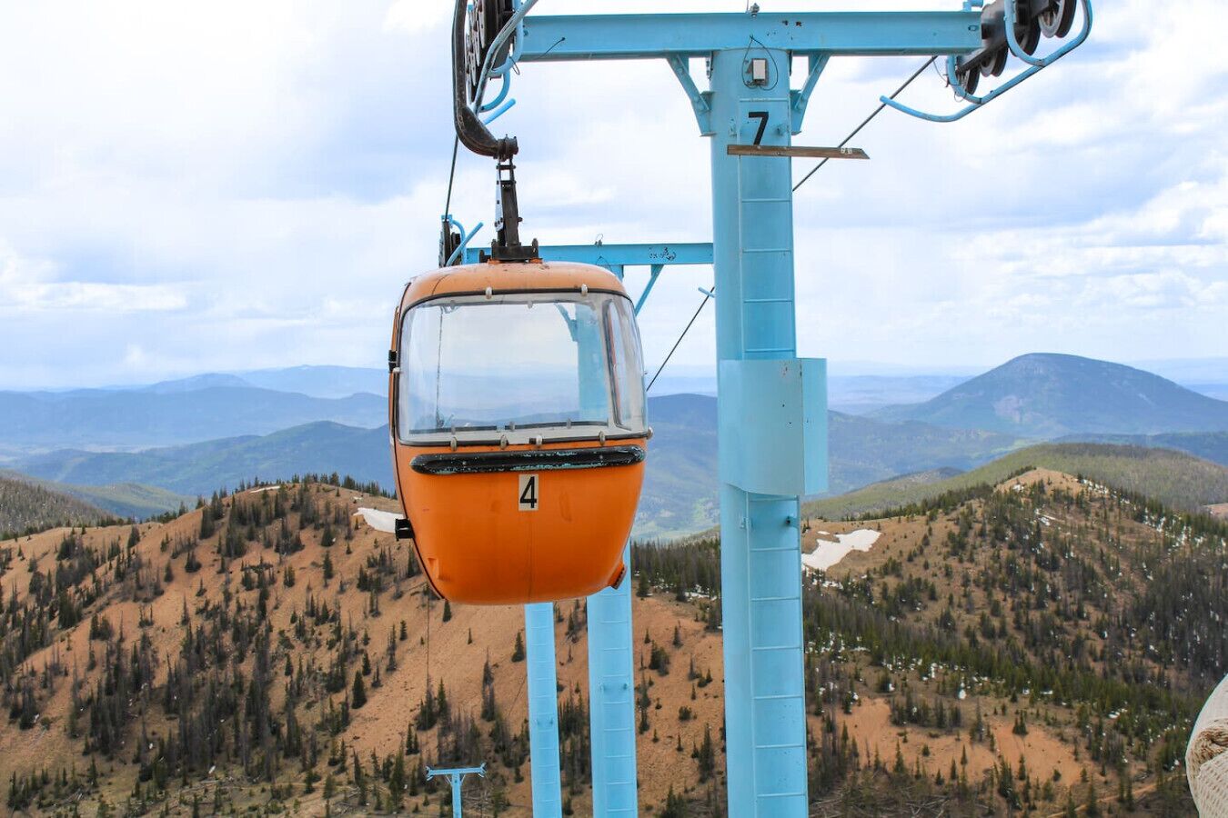 A cable car with the number 4 suspended from a blue cable system, overlooking a mountainous landscape with sparse vegetation.