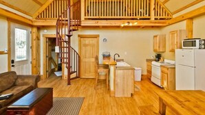 A cozy cabin interior with a wooden staircase, a kitchen with basic appliances, and a living area with a couch and a coffee table. - Treehouse 3 - Mourning Dove Haus by Best Texas Travel (New Braunfels)