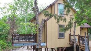A treehouse with a deck and a small attached cabin, surrounded by trees and a dirt path. - Treehouse  2 - Cardinal Casita by Best Texas Travel (New Braunfels)