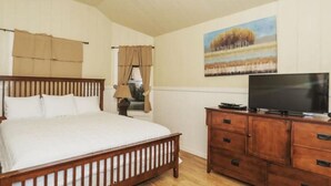 A bedroom with a wooden bed, a TV on a wooden cabinet, and a painting on the wall. - Treehouse  2 - Cardinal Casita by Best Texas Travel (New Braunfels)