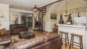 A spacious living room with leather sofas, a wooden coffee table, and a staircase leading to a kitchen area with a bar. - Treehouse  2 - Cardinal Casita by Best Texas Travel (New Braunfels)