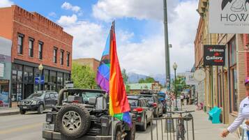 A street with a rainbow flag, a Jeep, and a storefront with a sign that reads 'HOW'.