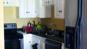 Una cocina compacta con gabinetes blancos, un refrigerador de acero inoxidable, una estufa y un lavavajillas.