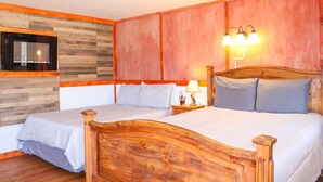 Ein Schlafzimmer mit zwei Betten, einem Holzkopfteil, einem an der Wand montierten Fernseher und einem Nachttisch mit Lampe.