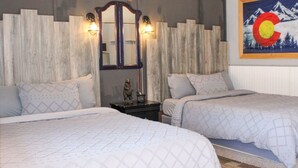 Une chambre d’hôtel avec deux lits, une tête de lit en bois, un miroir et un luminaire fixé au mur.