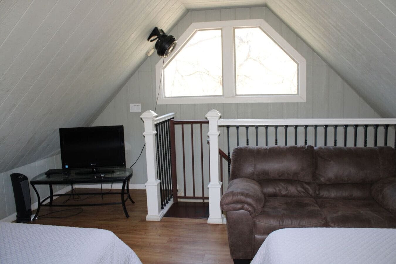 A cozy attic bedroom with a large window, a TV, and a leather sofa.