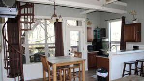 A spacious kitchen with wooden cabinets, a dining area with a table and chairs, and a spiral staircase. - Treehouse 5 - Robins Roost by Best Texas Travel (New Braunfels)