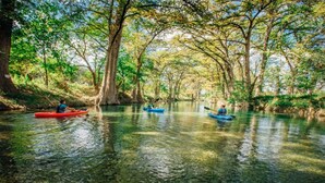 A calm river with kayaks, surrounded by trees and clear water. - Treehouse 5 - Robins Roost by Best Texas Travel (New Braunfels)