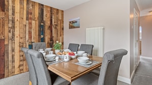 A dining room with a wooden wall, a table set for six, and grey upholstered chairs. - Roslen - Lovely Bungalow Near Beach and Village (Saundersfoot)