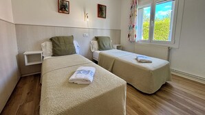 A room with two single beds, a small bedside table, a nightstand, a radiator, and a window with curtains.
