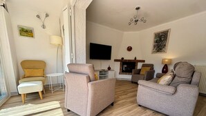 A living room with two armchairs, a sofa, a small table, a TV, and a fireplace.