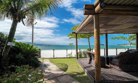 A beach view with a wooden pergola, a pathway, and a sign indicating access to the beach.. JBM Apto pé na areia com vista mar