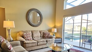 A living room with a sofa, two armchairs, a glass coffee table, a decorative mirror, and a view of a swimming pool through large windows. - 4 Bedroom and 3 Bath Home in the Highly Rated Community of Solana! (Davenport)