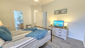 Une chambre à coucher avec un lit, des tables de chevet, un téléviseur et une salle de bain visible à travers une porte ouverte.