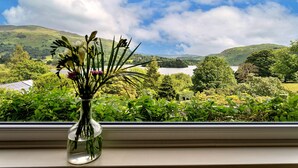 Una ventana con un jarrón de flores, que da a un paisaje pintoresco con colinas y un lago.