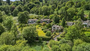 Una zona residencial con casas rodeadas de abundante vegetación y una colina al fondo.