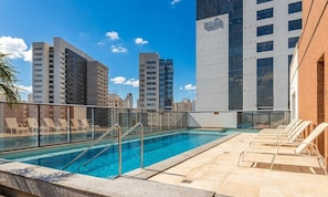 Une piscine sur le toit, dotée de chaises longues, d’une rambarde en verre et offrant une vue sur la ville.