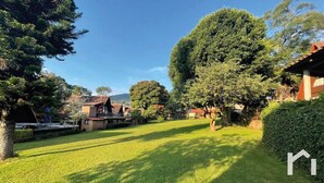 Un jardin bien entretenu, avec une pelouse, des arbres et un bâtiment doté d’un toit rouge.