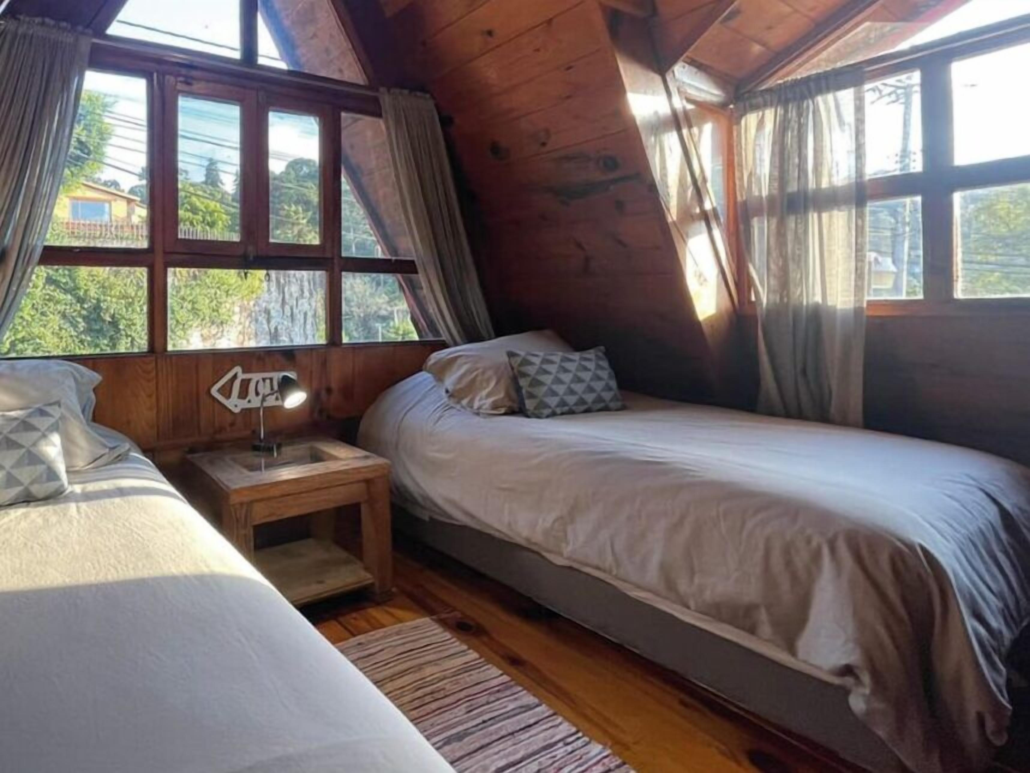 A cozy cabin room with two beds, wooden walls, and large windows.