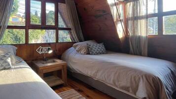 A cozy cabin room with two beds, wooden walls, and large windows.