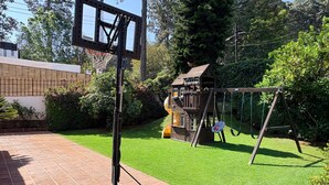 A basketball hoop, a swing set, and a small wooden playhouse in a backyard. - Incredible Property with Huge Garden and Pool! (Valle de Bravo)