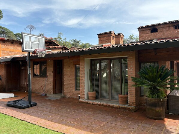 A brick house with a basketball hoop, potted plants, and a clear sky.