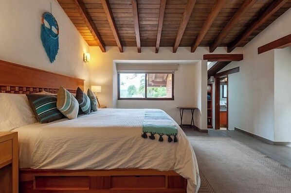 Un dormitorio con una cama de madera, una ventana y una puerta que da a otra habitación.
