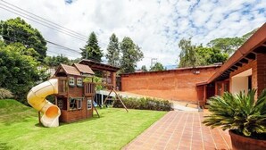 A backyard with a wooden playhouse, a slide, and a brick wall. - Incredible Property with Huge Garden and Pool! (Valle de Bravo)