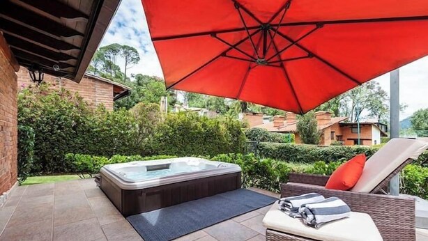A hot tub under a red umbrella, a wicker lounge chair, and a tiled patio area. - Incredible Property with Huge Garden and Pool! (Valle de Bravo)