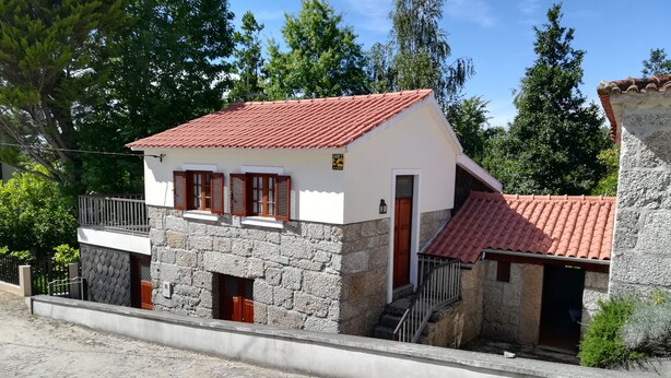 Una casa de piedra de dos plantas con techo de tejas rojas, contraventanas de madera y un pequeño balcón.