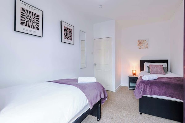 A hotel room with two beds, a nightstand with a lamp, and two framed abstract artworks on the wall.