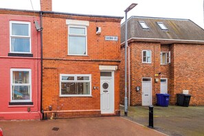 A red brick building with a white door and windows, a sign reading 'OXFORD ST.', and a blue trash bin on the pavement.