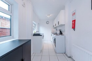 A narrow kitchen with white cabinets, a black countertop, and a window.