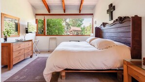 A bedroom with a wooden bed, a dresser, a mirror, and a window with a view of greenery. - Casa Male (Valle de Bravo)