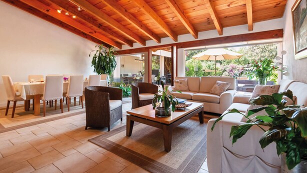 A spacious living area with a wooden ceiling, a dining table set for four, and a comfortable sofa facing a large window with a view of greenery. - Casa Male (Valle de Bravo)