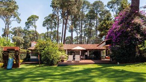 A house with a patio, a play area, and a garden with trees and purple flowers. - Casa Male (Valle de Bravo)