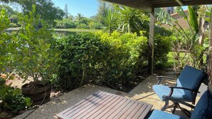 A covered patio area with a wooden table and chairs, surrounded by lush greenery and a view of a garden and a pond. - Siesta Key Newly Renovated Condo with Private Beach/short walk to Siesta Village (Siesta Key)