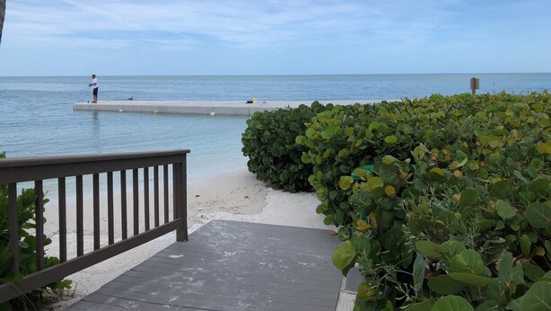 A wooden deck leading to a beach with a concrete pier extending into the water. - Siesta Key Newly Renovated Condo with Private Beach/short walk to Siesta Village (Siesta Key)