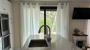A modern kitchen with a large island, built-in ovens, and a window with curtains. - Siesta Key Newly Renovated Condo with Private Beach/short walk to Siesta Village (Siesta Key)