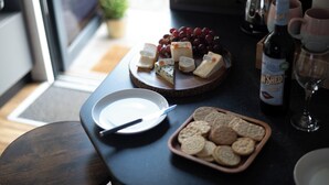 Una mesa con queso, uvas, galletas, una botella de vino y una copa sobre una encimera oscura.